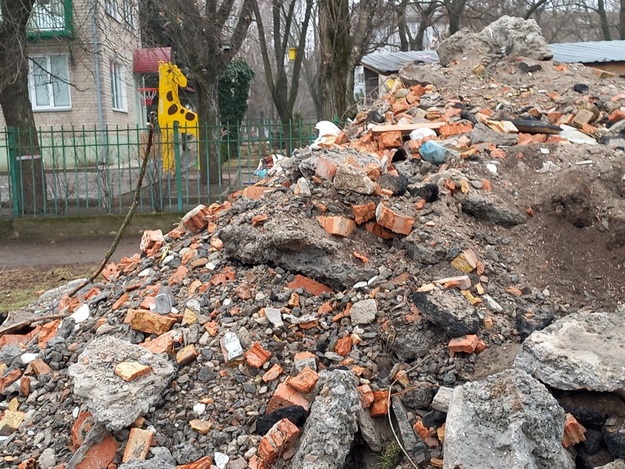 Куча строительного мусора на фоне детской площадки во дворе многоквартирного дома