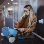 Дівчина працює у громадському місці на ноутбуці, який підключений до розетки